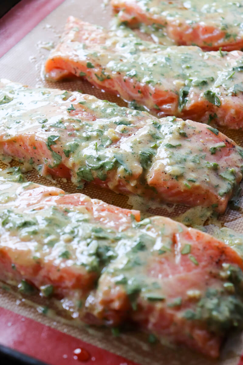 Front view of a pan of 4 raw servings of keto salmon on a silicone baking mat ready to go in the oven
