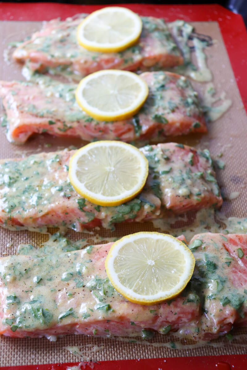 Front view of a pan of 4 raw servings of keto salmon with lemon slices on a silicone baking mat ready to go in the oven