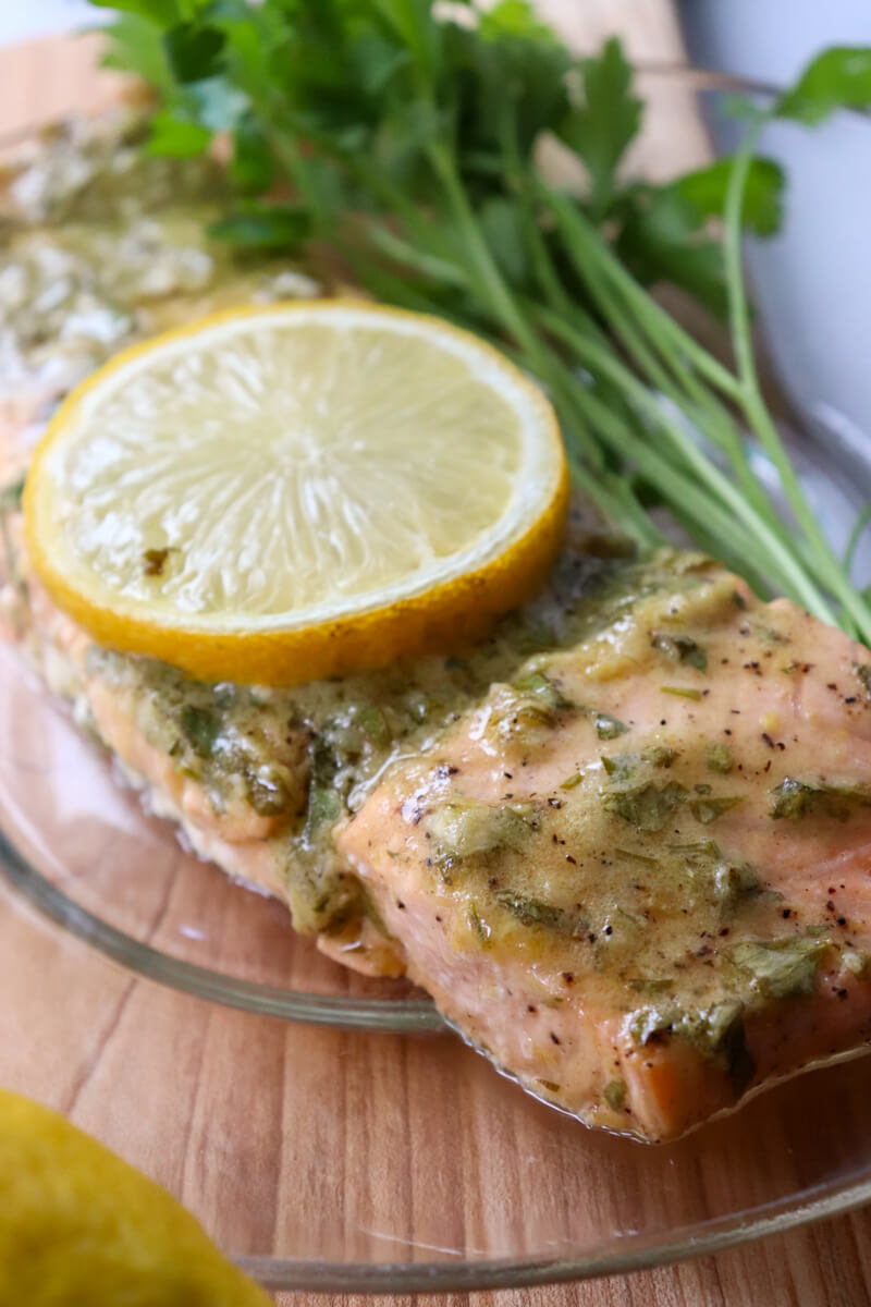 Front overhead close up of a serving of keto baked salmon with a lemon dijon sauce on a glass plate on a wooden cutting board