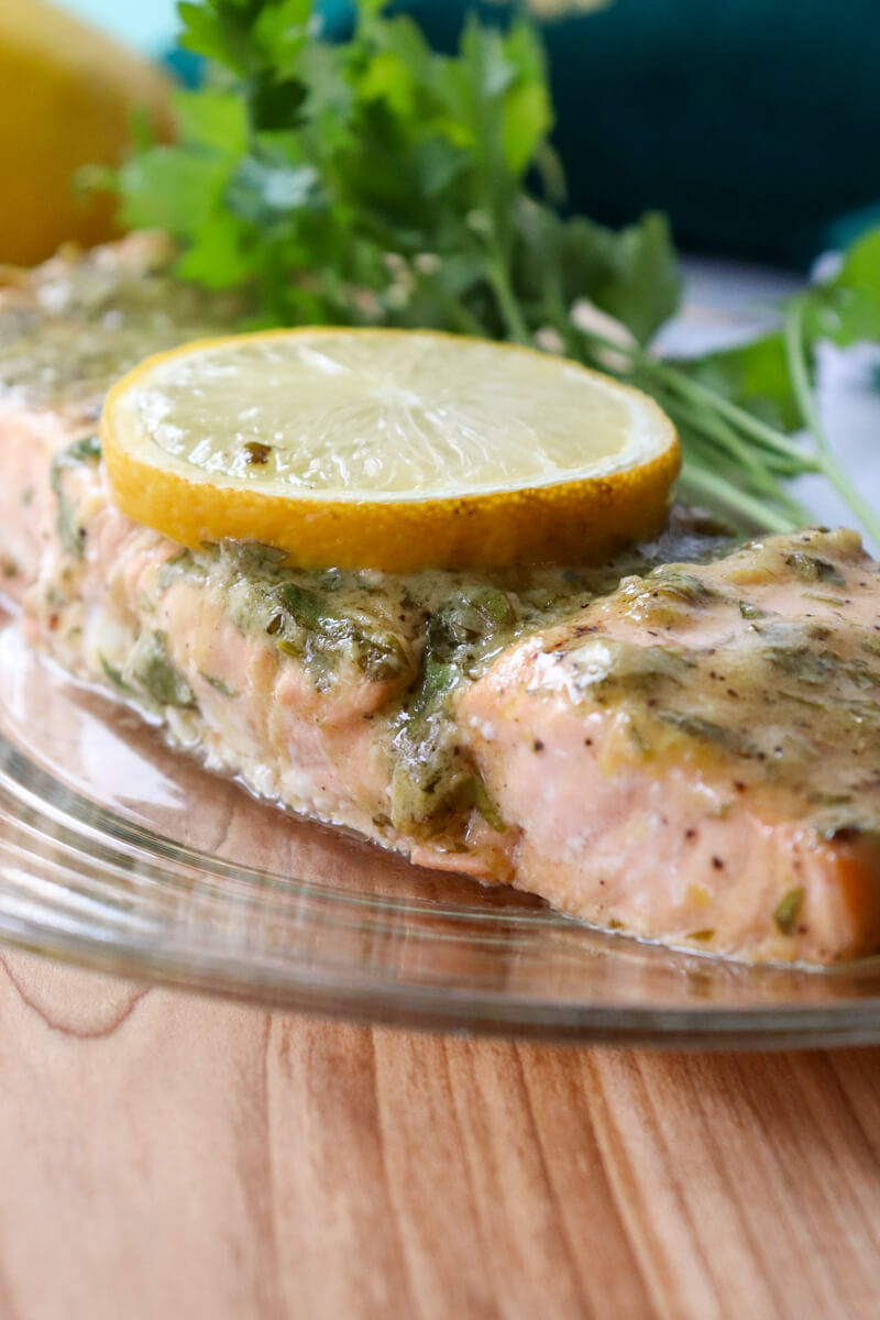 Front close up of a serving of keto baked salmon with a lemon dijon sauce on a glass plate on a wooden cutting board