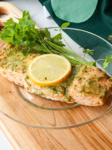 Serving of keto baked salmon with a lemon dijon sauce on a glass plate on a wooden cutting board