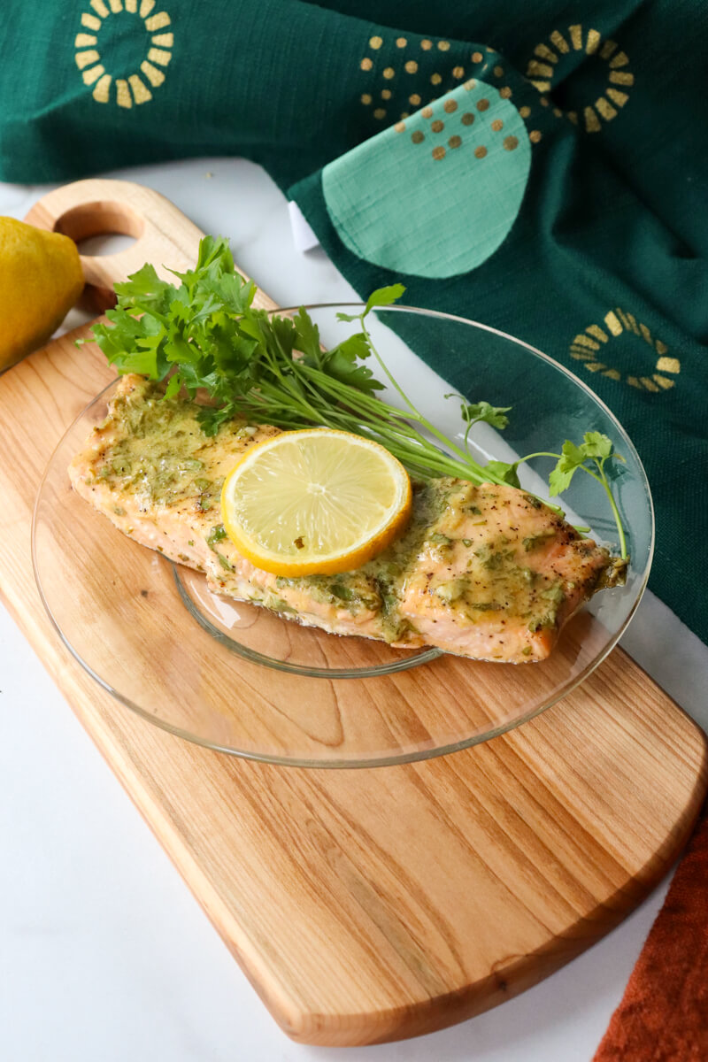 Serving of keto baked salmon with a lemon dijon sauce on a glass plate on a wooden cutting board