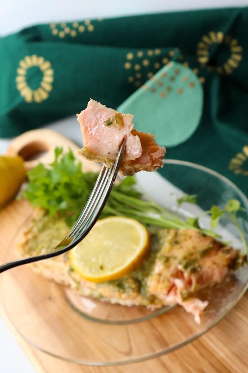 A piece of keto salmon on a fork in front of a glass plate with a serving