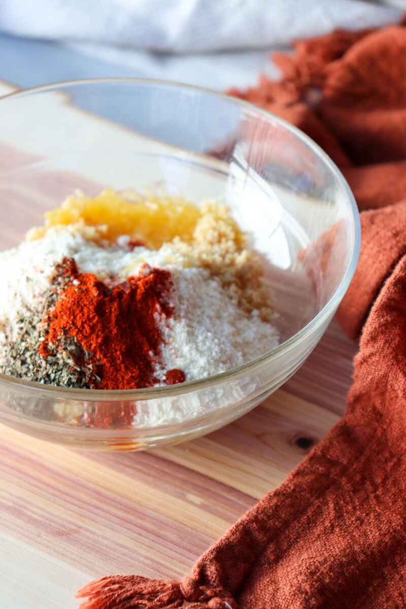 A glass bowl with salt, pepper, paprika, butter, crushed pork rinds, the ingredients for the chicken cordon bleu casserole topping