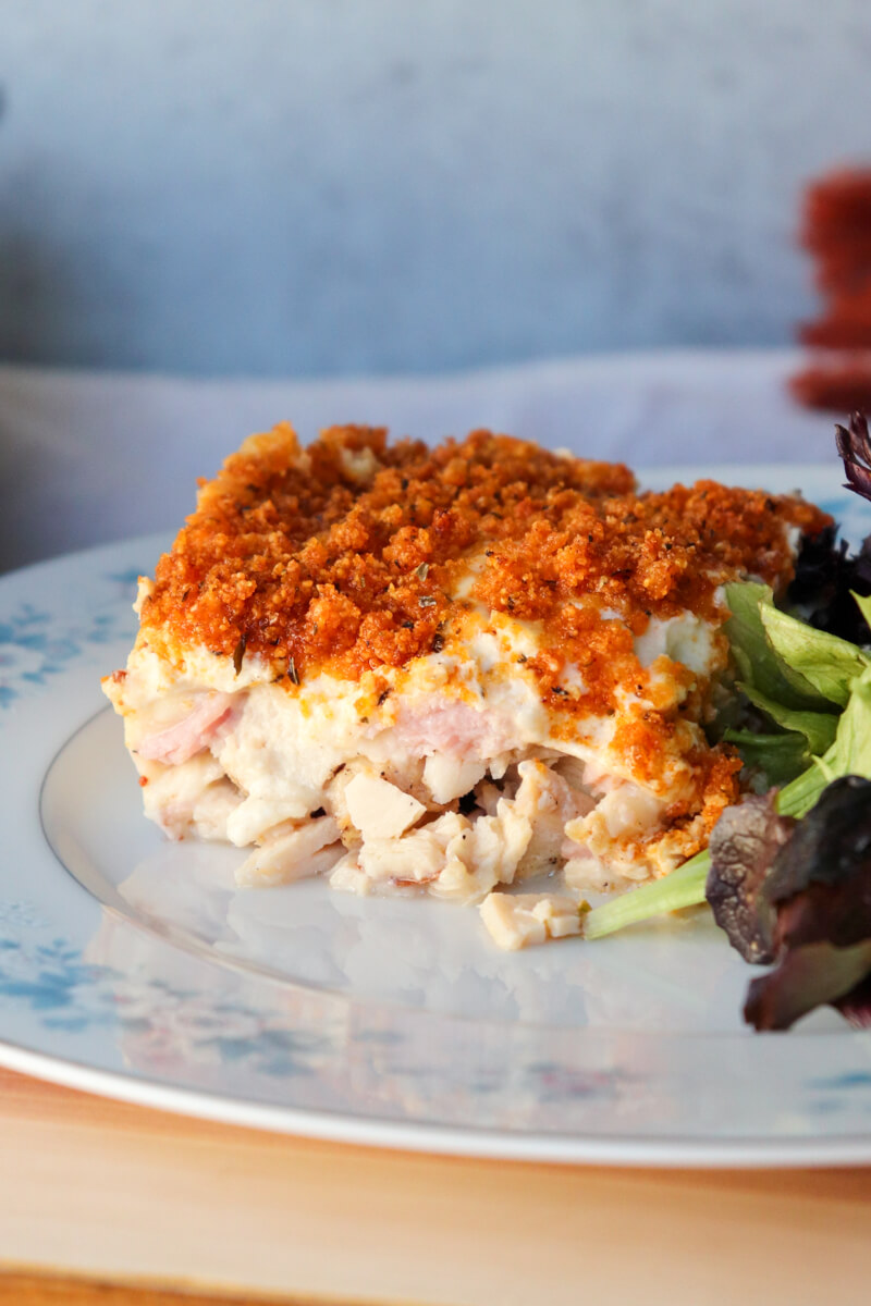 Slice of keto chicken cordon bleu casserole with crispy pork rind topping served on a plate with mixed greens salad.