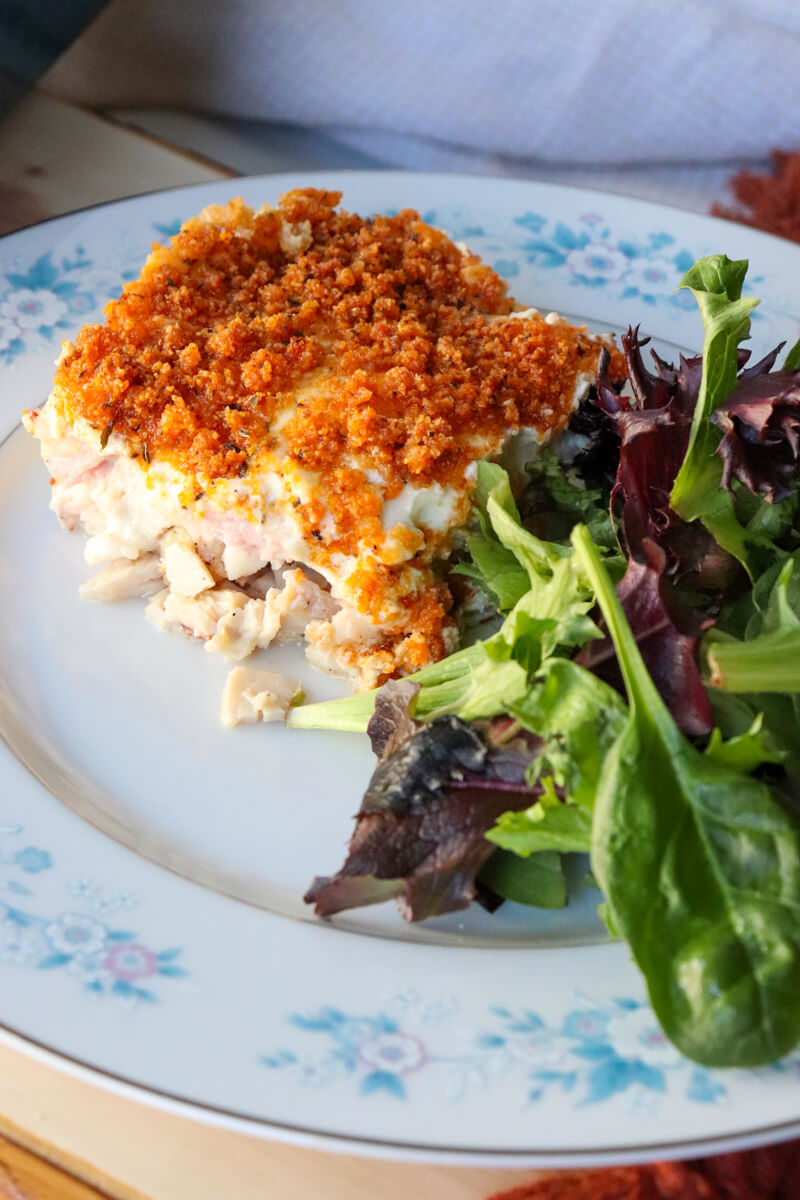 Slice of keto chicken cordon bleu casserole with crispy pork rind topping served on a plate with mixed greens salad.