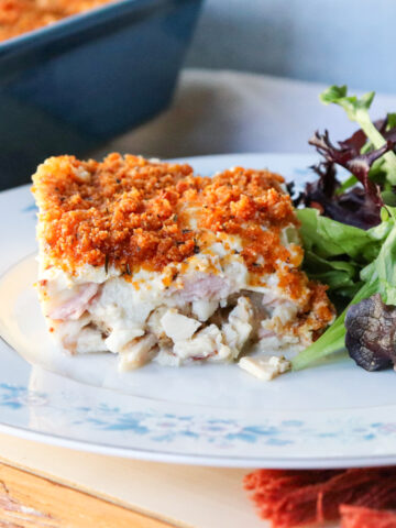 Slice of keto chicken cordon bleu casserole with crispy pork rind topping served on a plate with mixed greens salad.
