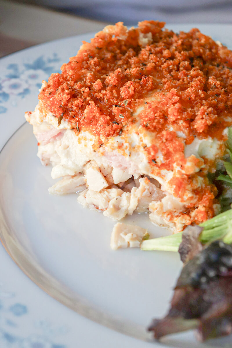Slice of keto chicken cordon bleu casserole with crispy pork rind topping served on a plate with mixed greens salad.