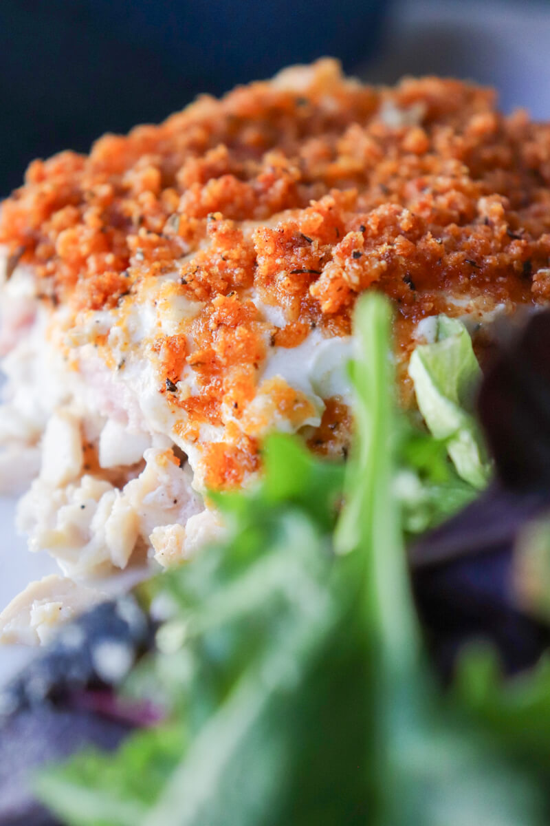 A closeup of a serving of chicken cordon bleu casserole with blurred greens in front