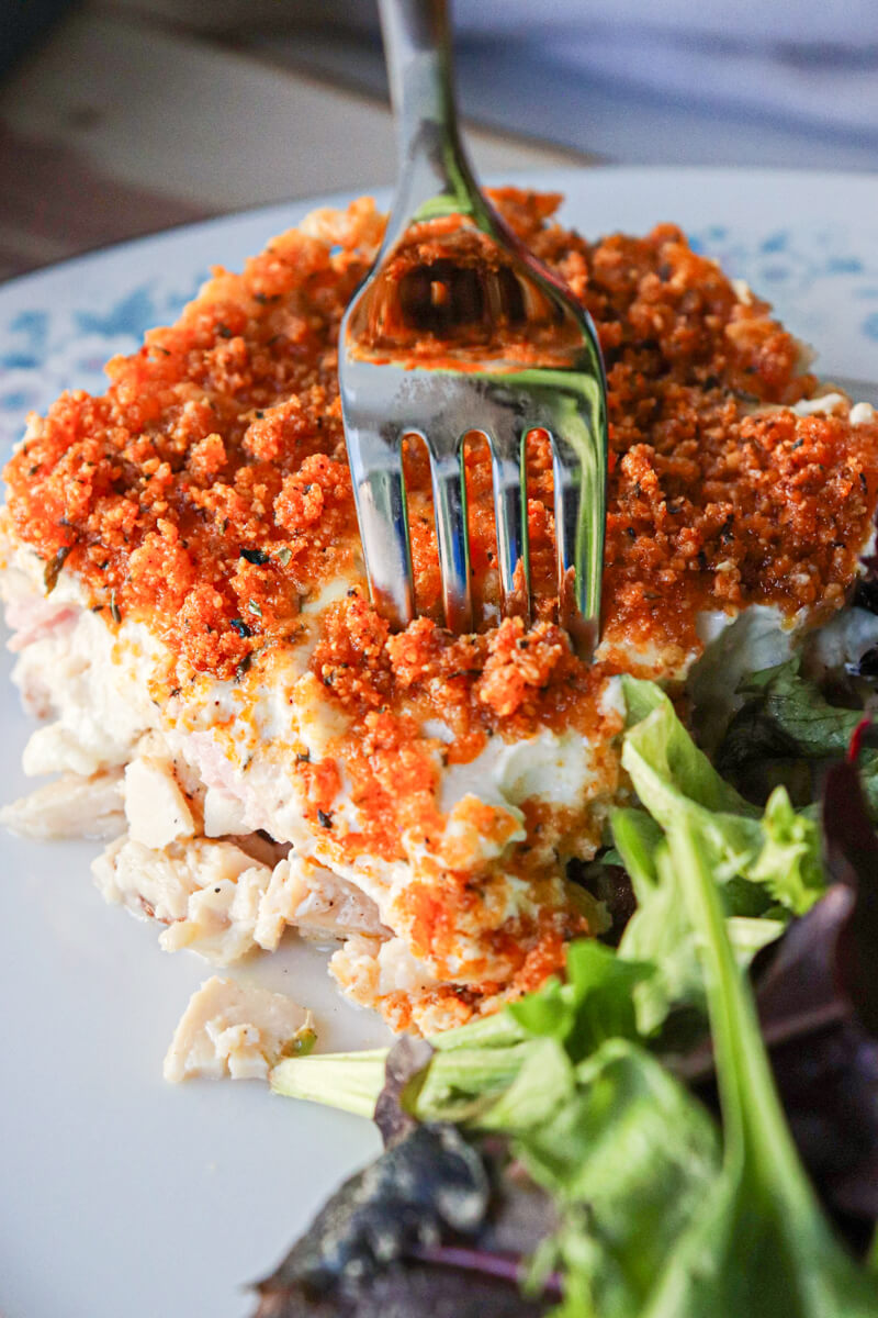 A fork in a serving of low carb chicken cordon bleu casserole with greens in the front