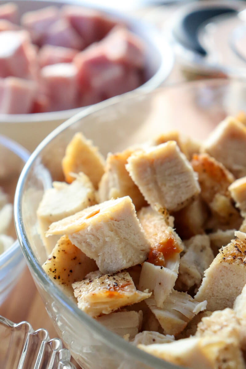 Glass bowl with diced chicken pieces in front of a white bowl of ham