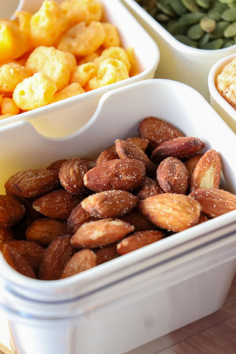 Close-up of keto snack containers with almonds, Moon Cheese, and green pumpkin seeds arranged in a divided tray for a low carb movie snack setup