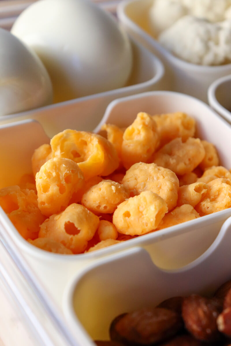 Close-up of keto snack containers with Moon Cheese, almonds, and boiled eggs arranged in a divided tray for a low carb movie snack setup