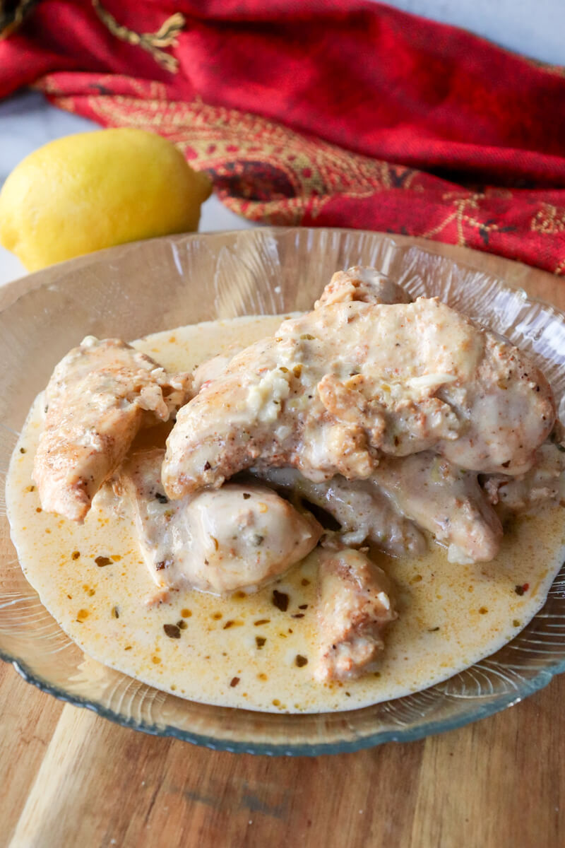 A textured glass plate of creamy lemon garlic chicken on a wooden board.