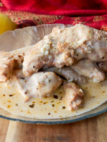 A textured glass plate of creamy lemon garlic chicken on a wooden board.