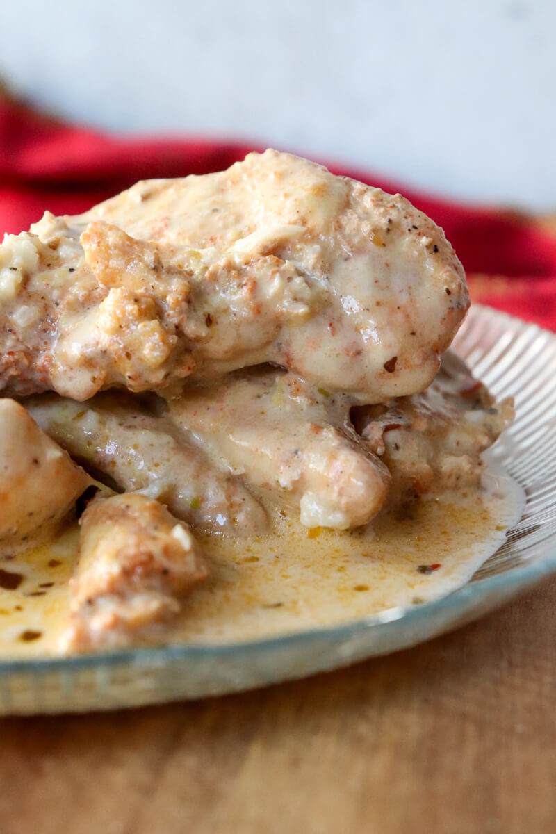 Front close up view of a textured glass plate of creamy lemon garlic chicken on a wooden board