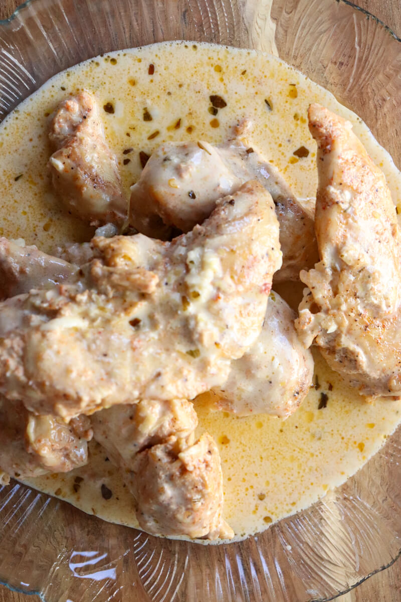 Overhead view of a textured glass plate of creamy lemon garlic chicken on a wooden board