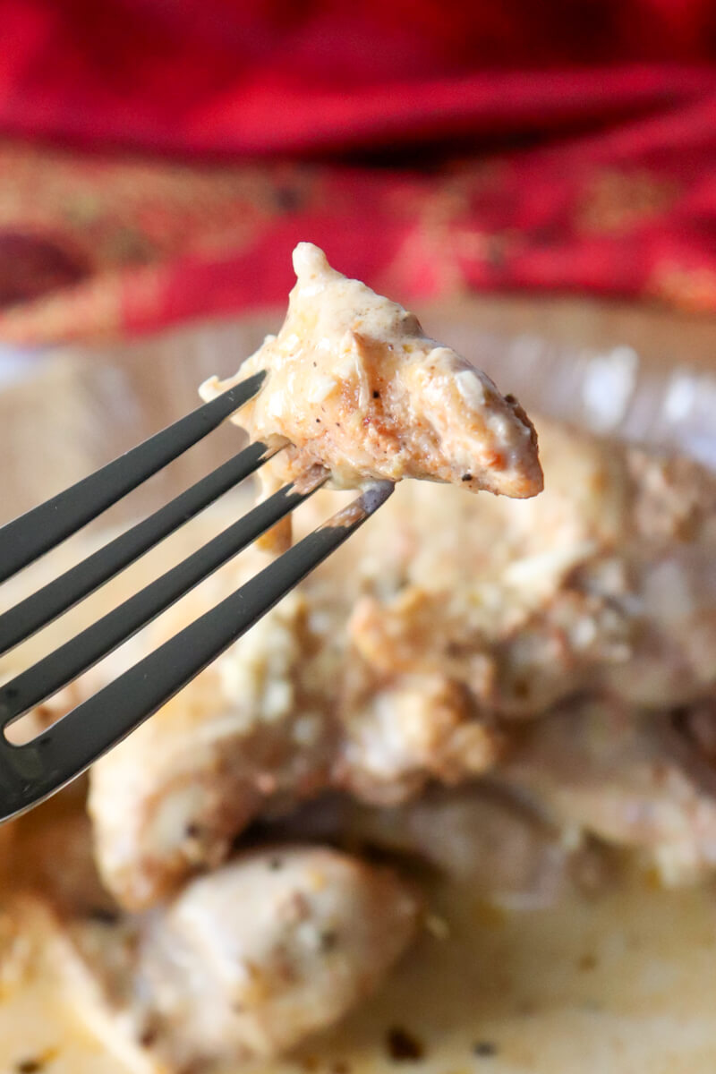 A fork holding up a bite of creamy lemon garlic chicken in front of a plate of the same.