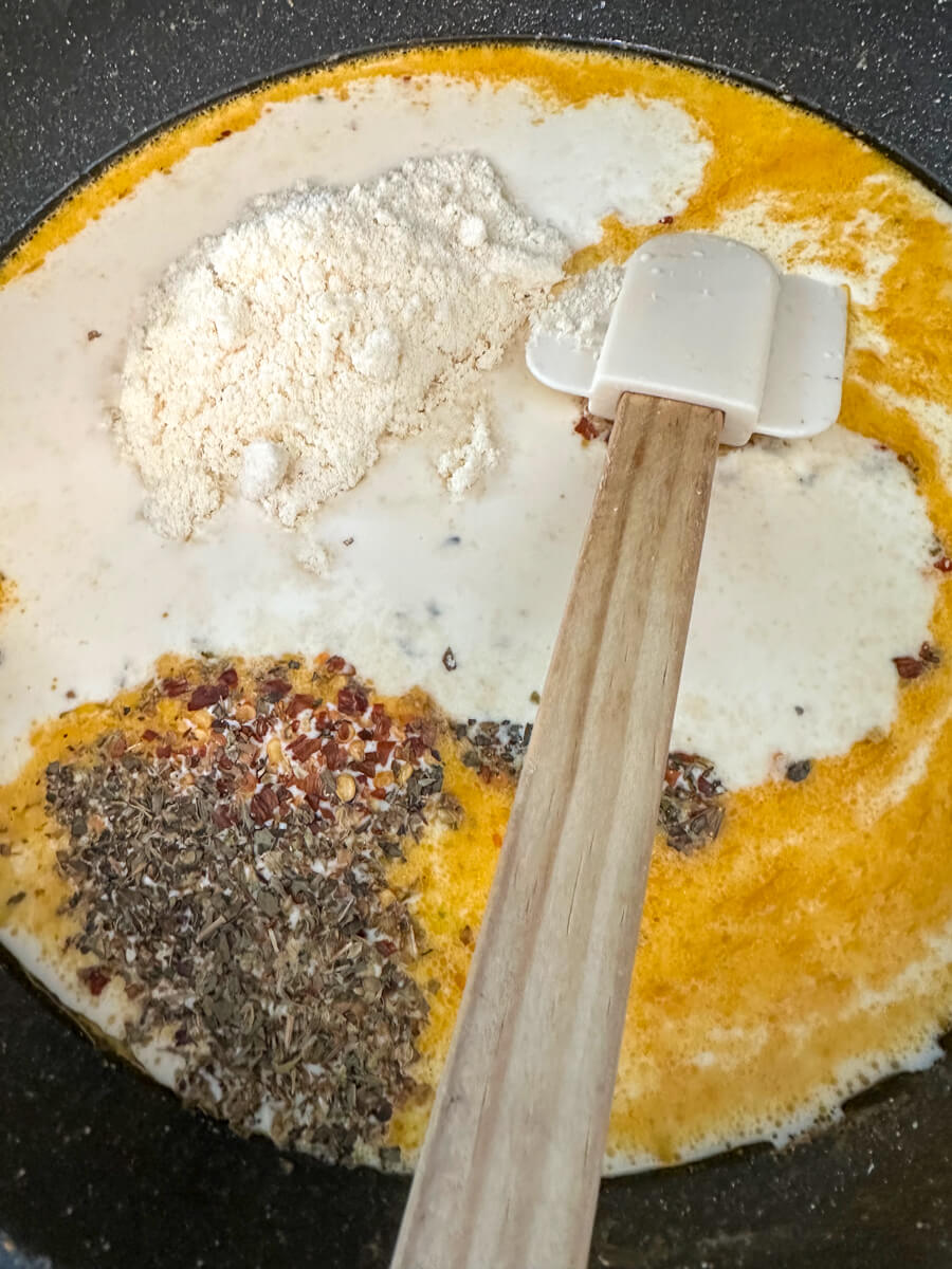 Front overhead view of a skillet with sauce ingredients, cream, melted butter, parmesan, spices, etc. and a spatula about to stir it together