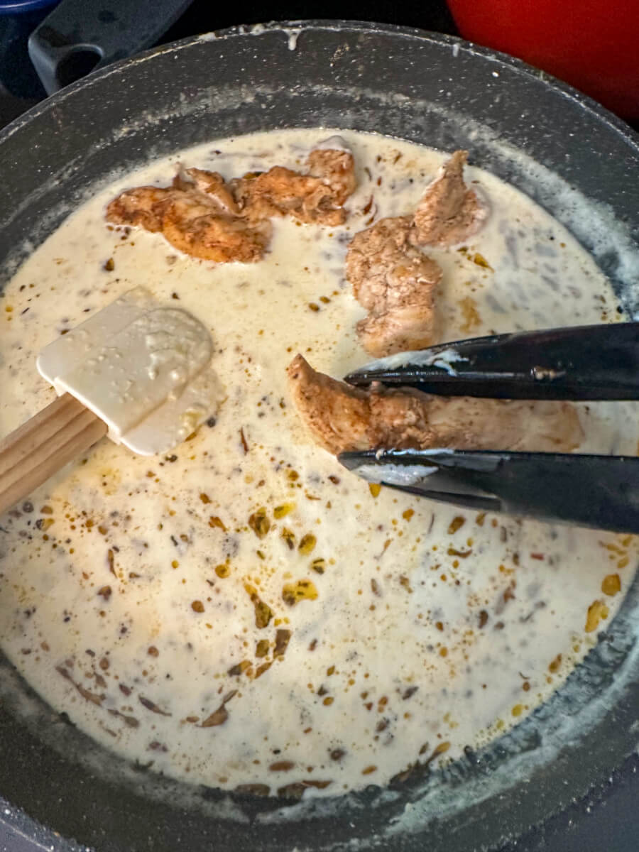 Overhead view of a skillet with creamy lemon garlic sauce and tongs putting pieces of chicken back into the pan