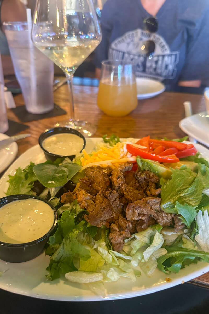 A plate of steak salad on a wooden table in front of some other drinks and plates
