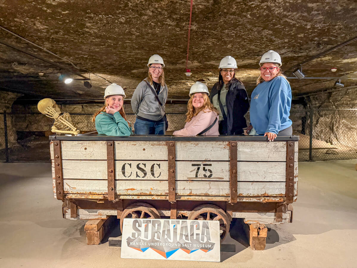 Five women in white hard hats in a a wood salt car imprinted CSC 75 on the side