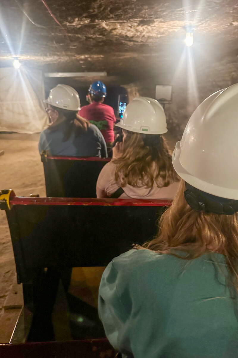 The train tour with the back heads of participants in white hard hats looking into the salt mine tunnels