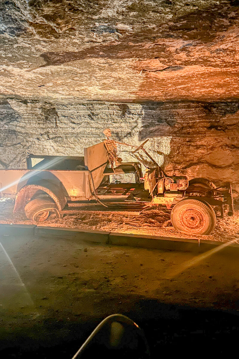 Underground in the Strataca salt mine exhibit with a view of an antique car with a skeleton riding in front, striations on the wall