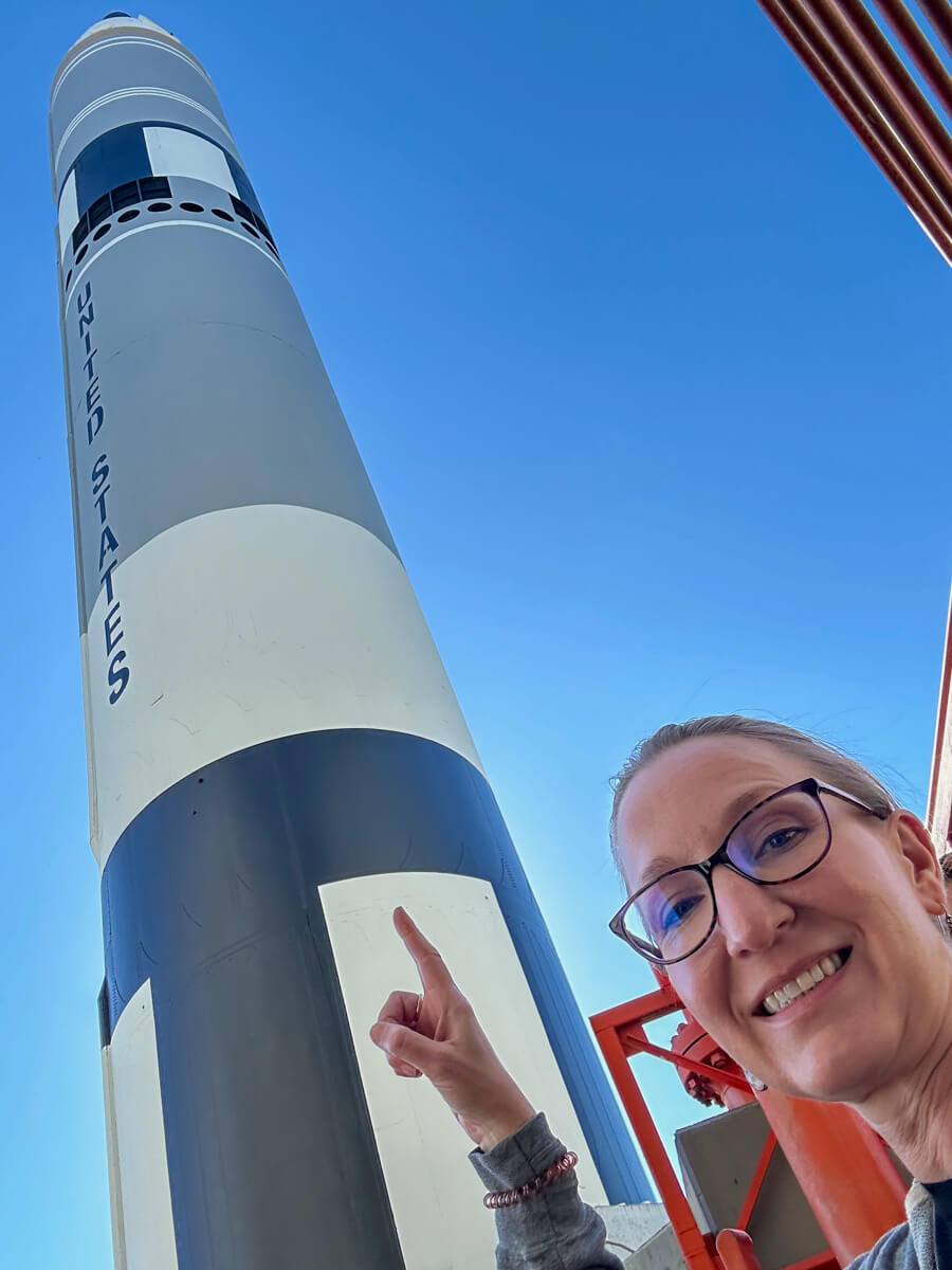 Outside looking up at the blue and white rocket on display with a woman in glasses pointing up to it