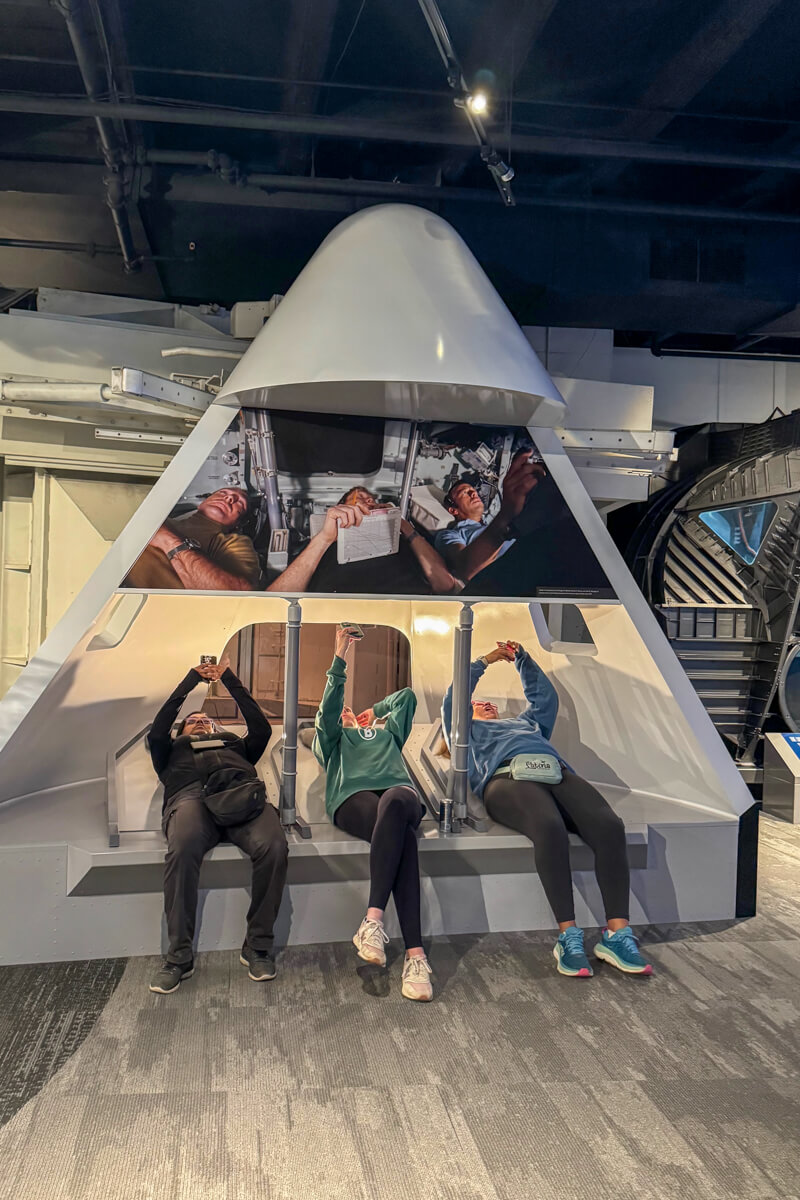 Interactive space capsule display with 3 women laying back in it looking up at the display