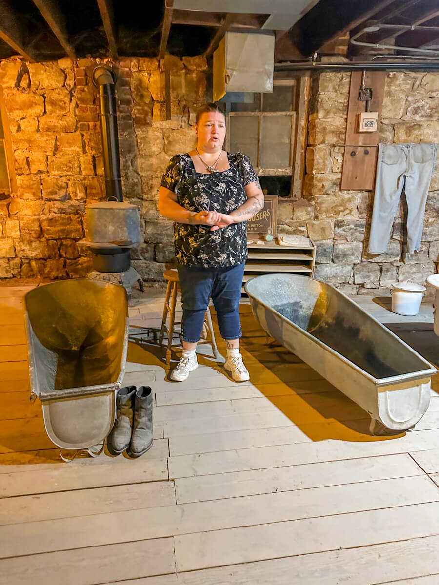A women standing in between two metal period bathtubs in the bath house area of the underground city in Ellinwood, Kansas