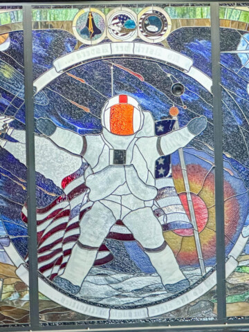 A stained glass window of an astronaut with flag and space background