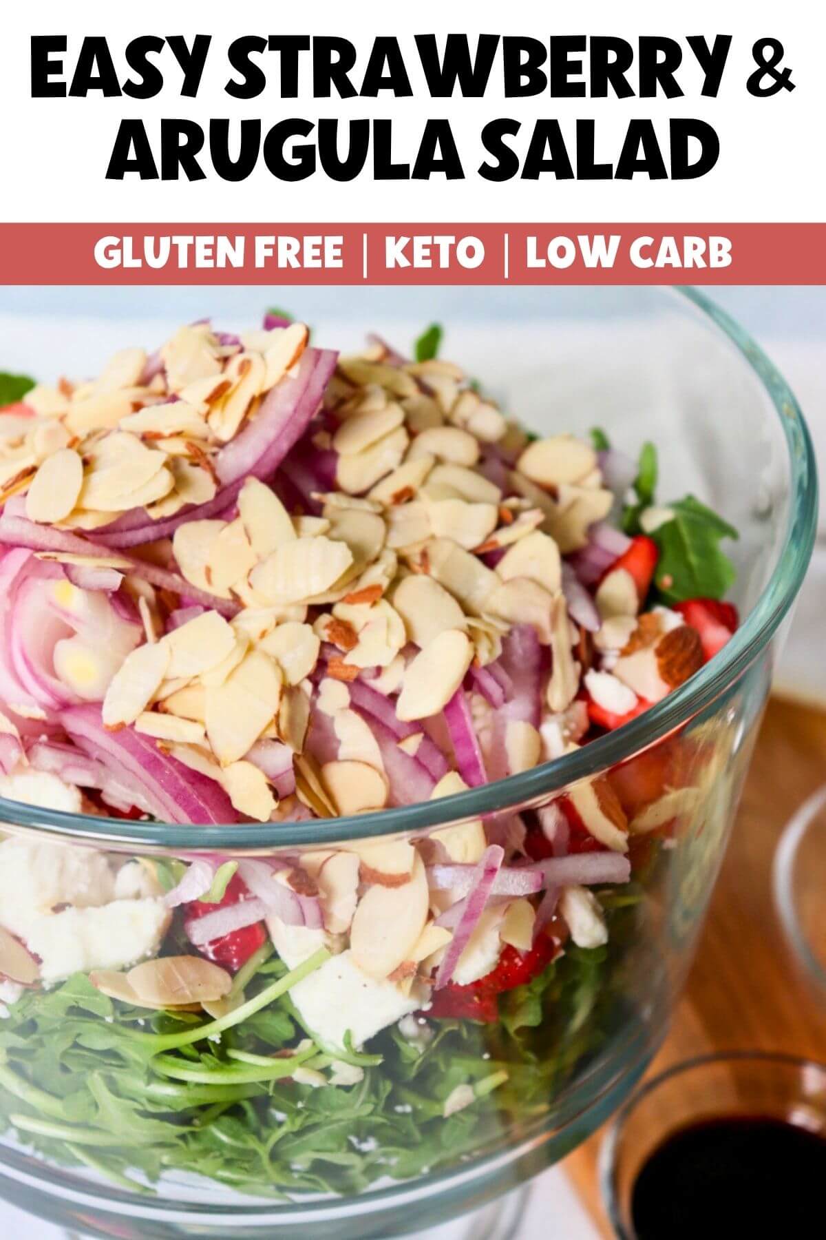 Arugula and Strawberry Salad with sliced almonds, red onion, goat cheese, and fresh strawberries in a large glass serving bowl.