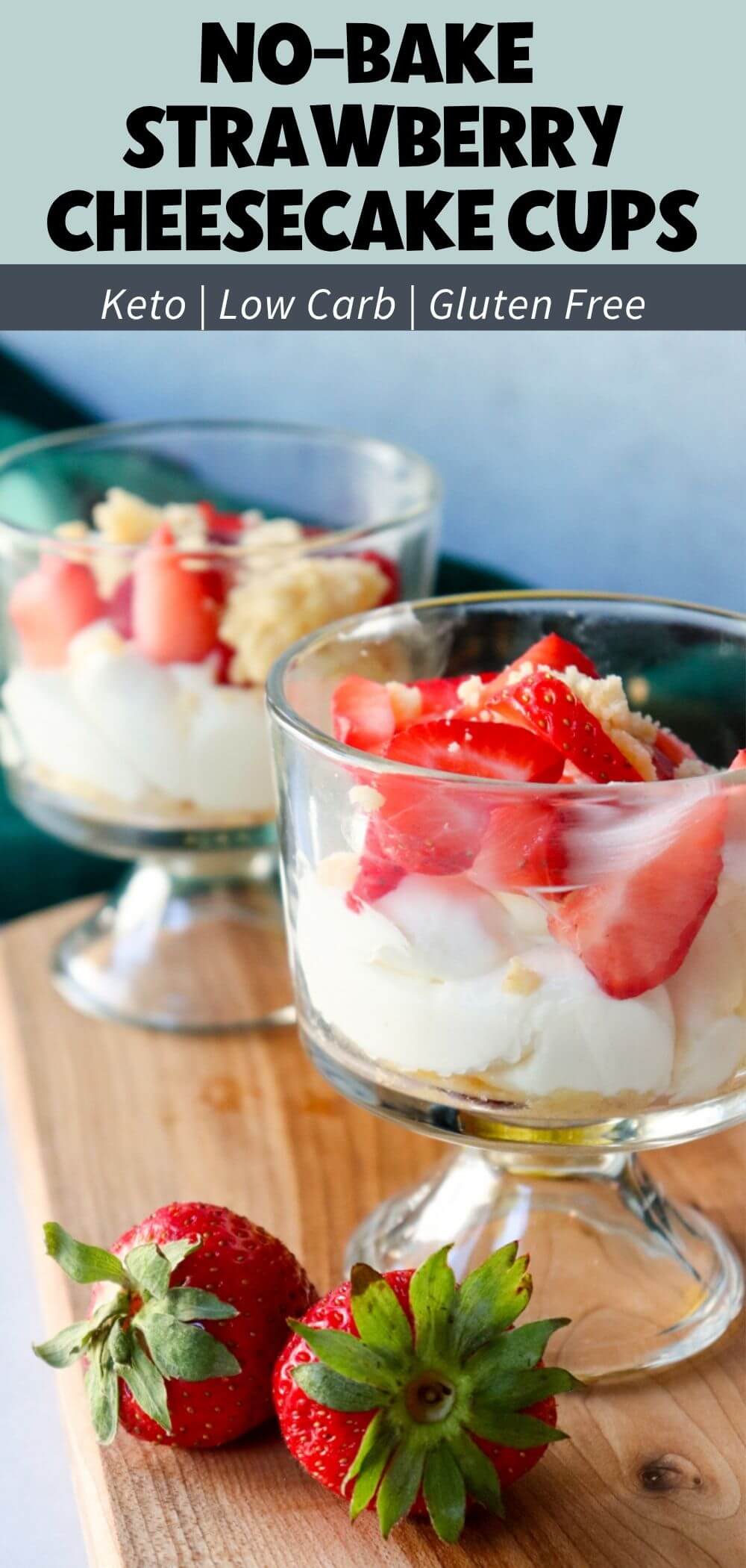 Two no-bake strawberry cheesecake cups topped with sliced strawberries and crumble topping on a wooden board with fresh strawberries.