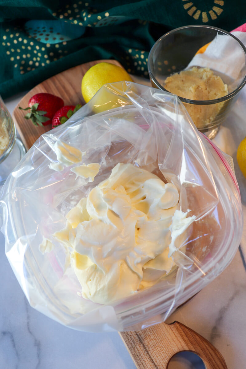 View of the whipped cream cheese filling in a plastic zipper bag next to some strawberries and a lemon.