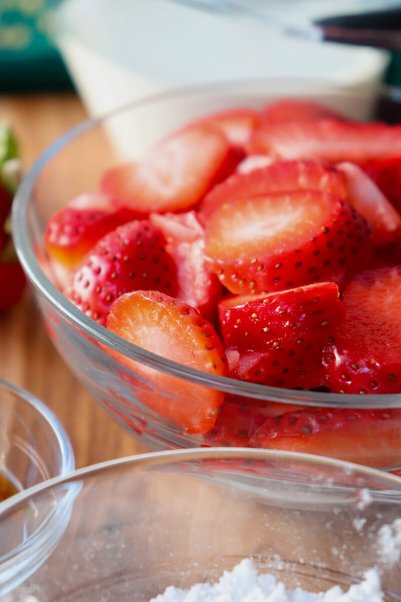 Close up view of a clear glass bowl of sliced strawberries.