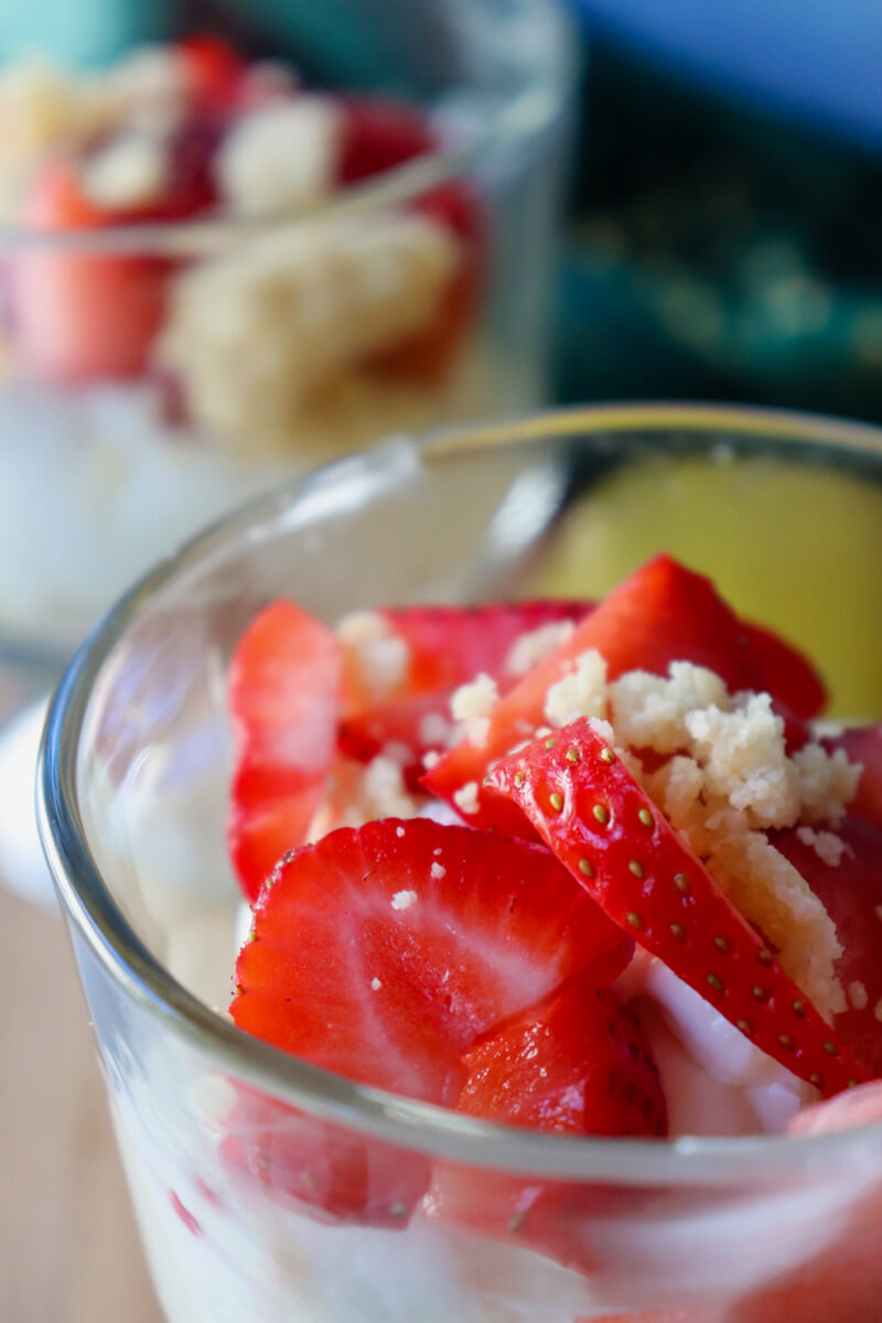 Close-up of keto no-bake strawberry cheesecake cup with creamy cheesecake filling, fresh strawberries, and almond flour crumble topping with another in the background.