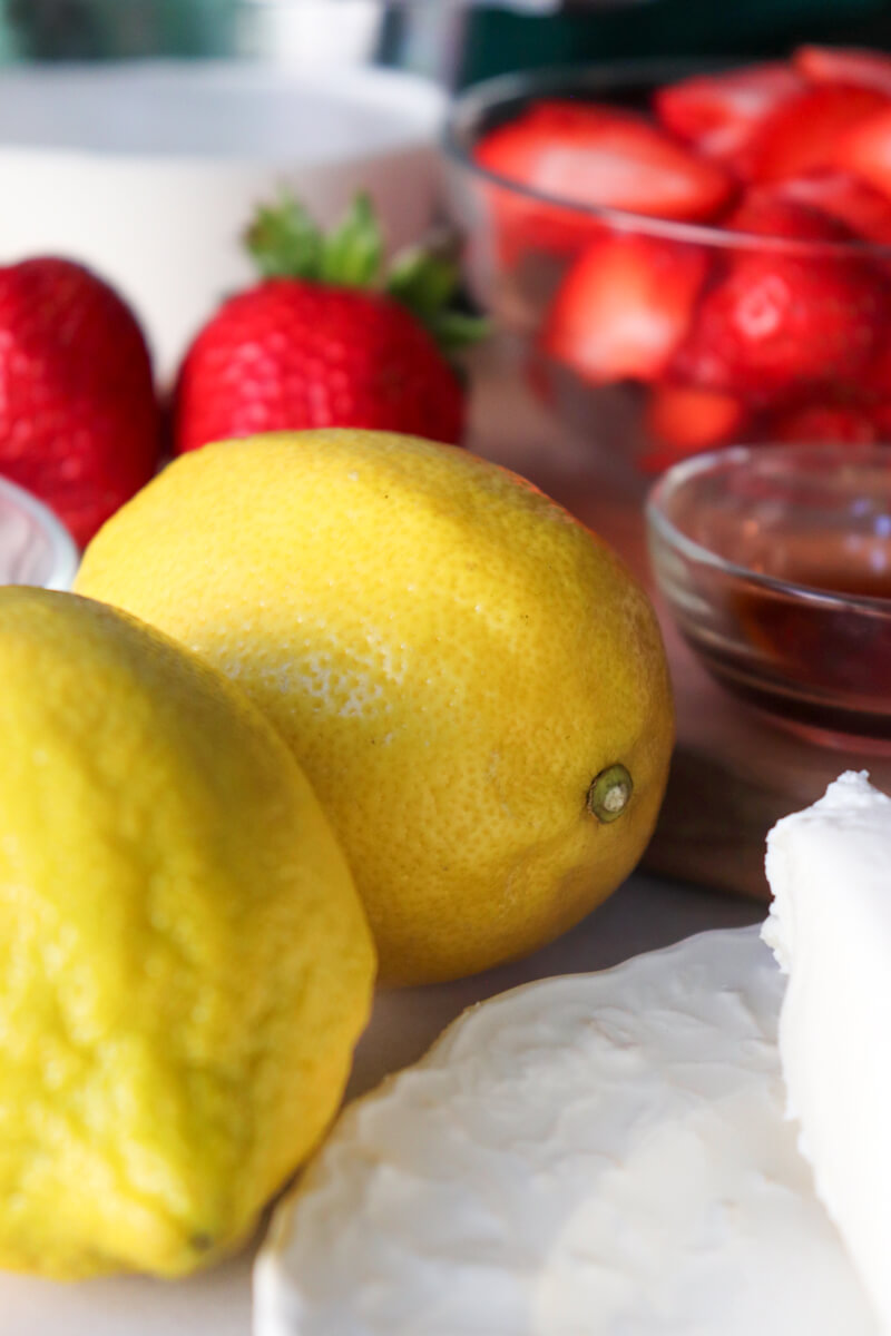 Close up view of two bright yellow lemons with strawberries in the background.