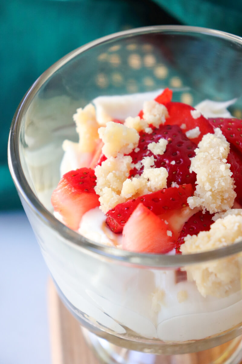 Close-up of keto no-bake strawberry cheesecake cup with creamy cheesecake filling, fresh strawberries, and almond flour crumble topping.