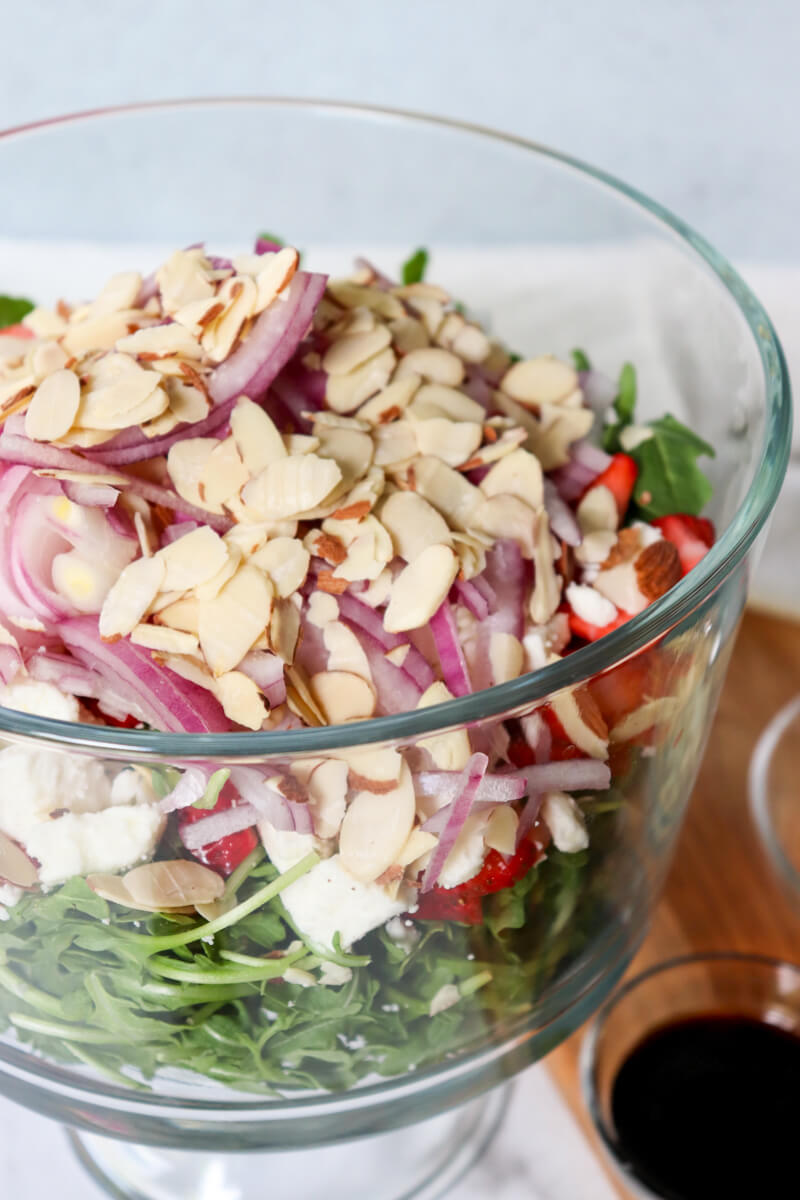 Arugula and Strawberry Salad with sliced almonds, red onion, goat cheese, and fresh strawberries in a large glass serving bowl.