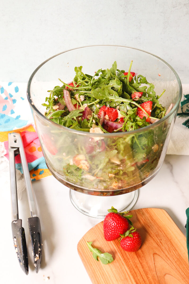 Front view of a glass bowl with Easy Strawberry Arugula Salad tossed with strawberries, arugula, almonds, red onion, and feta cheese for a low-carb spring side salad.