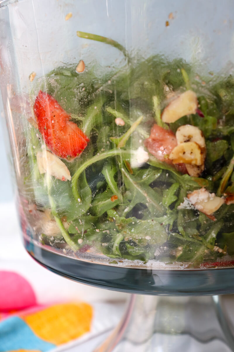 Side view of a glass bowl with Easy Strawberry Arugula Salad tossed with strawberries, arugula, almonds, red onion, and feta cheese for a low-carb spring side salad.