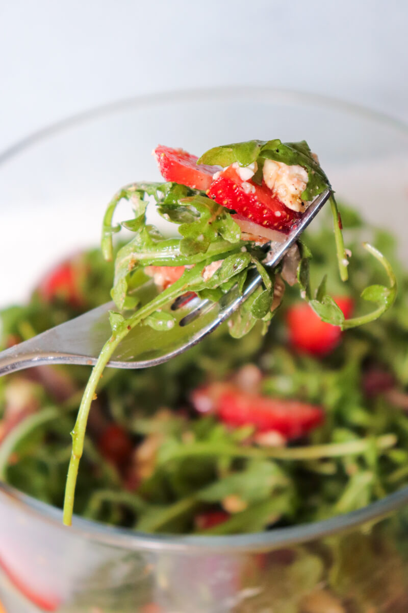 Forkful of Strawberry Arugula Salad with fresh arugula, sliced strawberries, goat cheese, and almonds in a low-carb gluten-free spring salad.