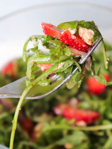 Forkful of Strawberry Arugula Salad with fresh arugula, sliced strawberries, goat cheese, and almonds in a low-carb gluten-free spring salad.