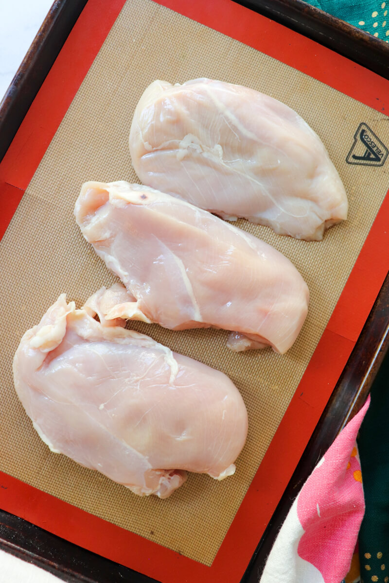 Overhead view of a sheet pan with three raw chicken breasts