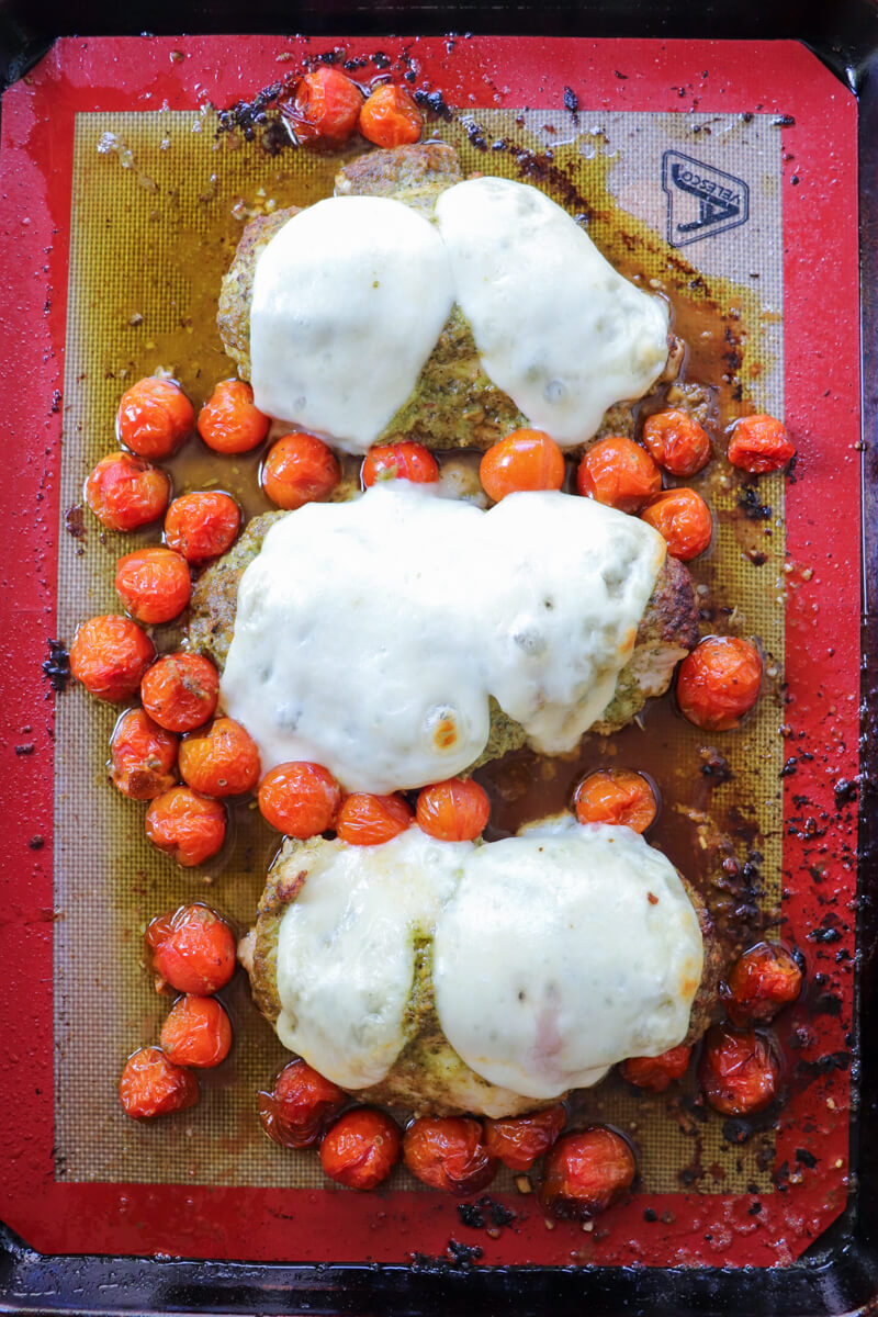 Overhead view of baked pesto chicken with tomatoes and mozzarella on the baking pan