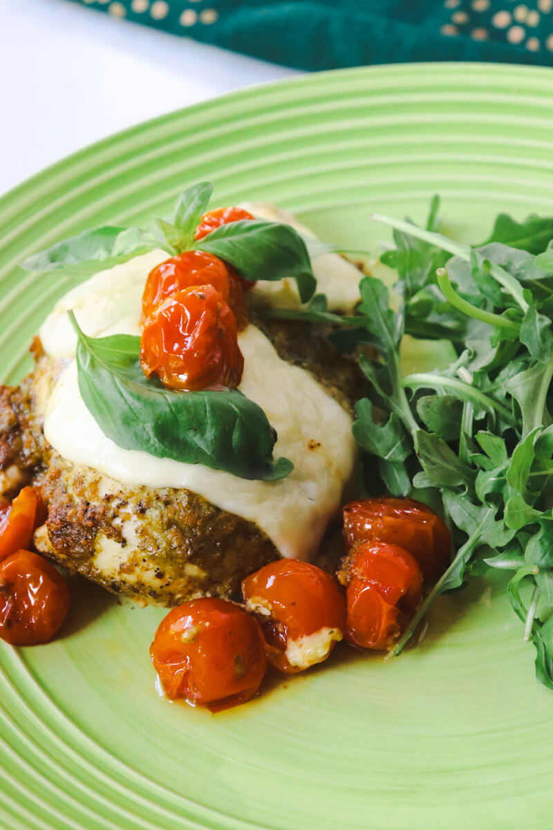 Keto Pesto Chicken with Roasted Tomatoes & Mozzarella on a light green plate with arugula in the background