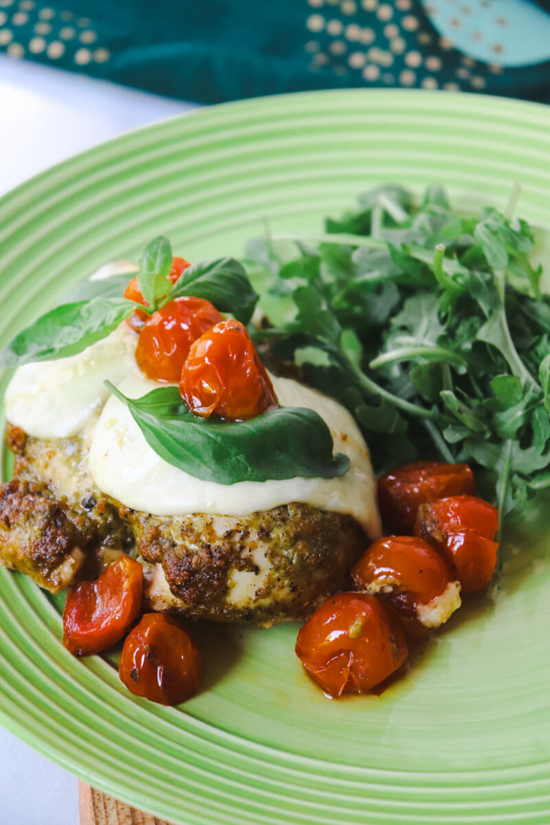 Low carb Pesto Chicken with Roasted Tomatoes & Mozzarella on a light green plate with arugula in the background