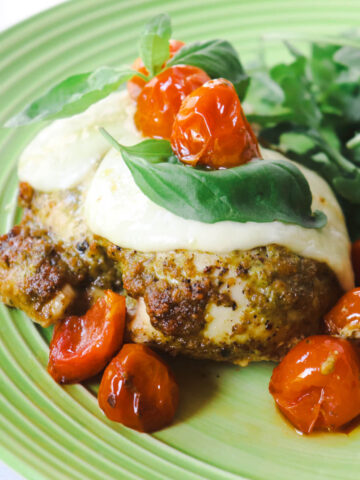 Pesto Chicken with Roasted Tomatoes & Mozzarella on a light green plate with arugula in the background